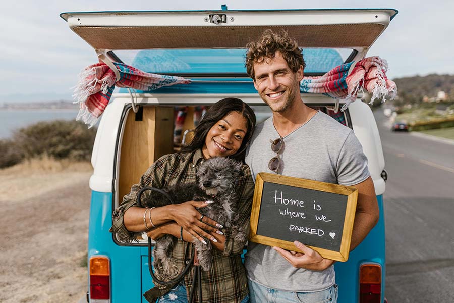 Couple by Campervan holding sign Home Is Where We Parked